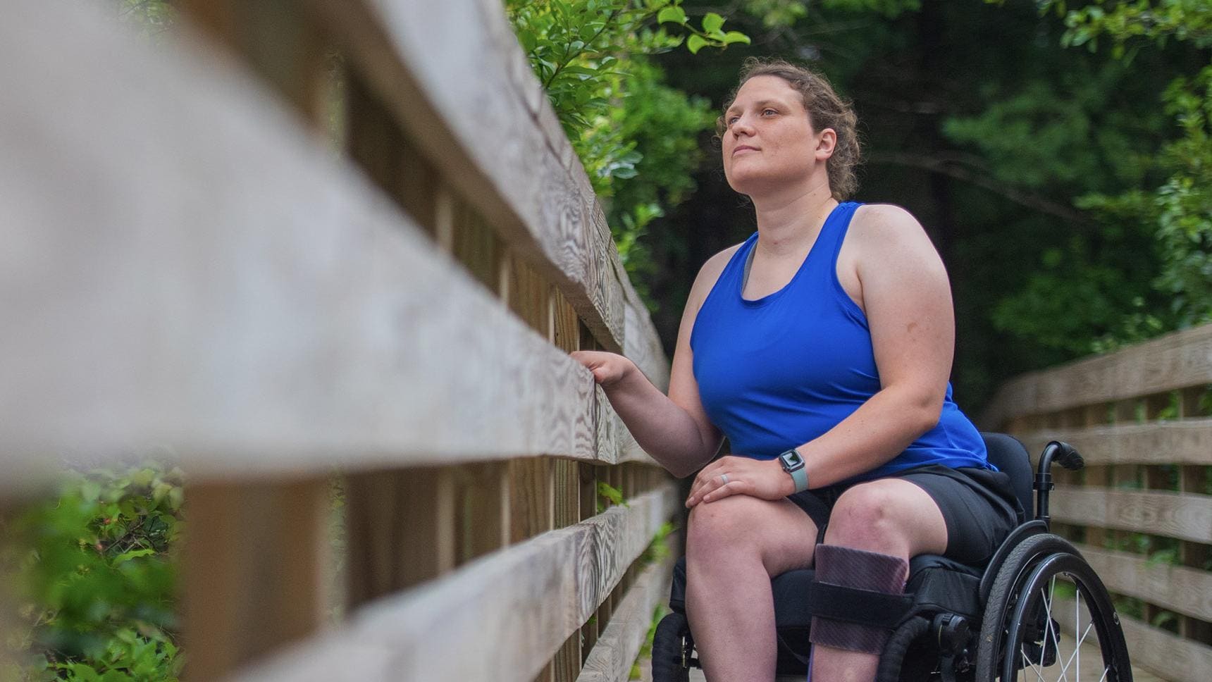 A person in a wheelchair on an outdoor bridge, gazing at the nature around them