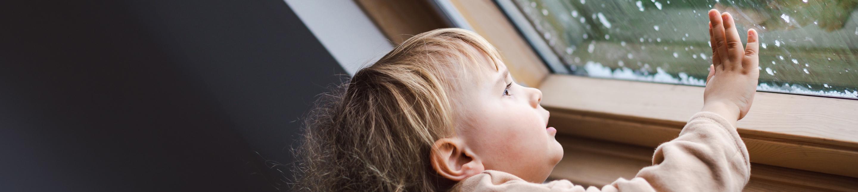 A young child staring out a rainy window and touching the glass