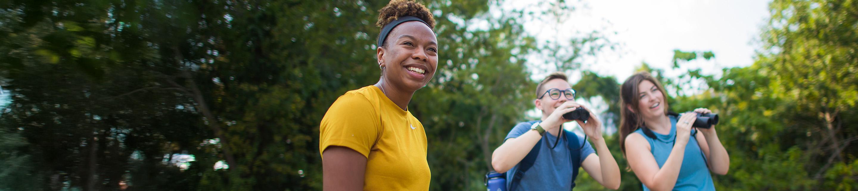 A group of people outdoors doing a nature walk, looking through binoculars