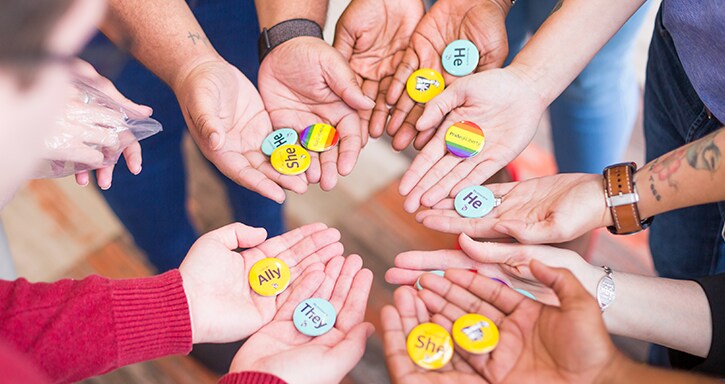 Group of hands holding different pins saying Ally, She, She, etc.