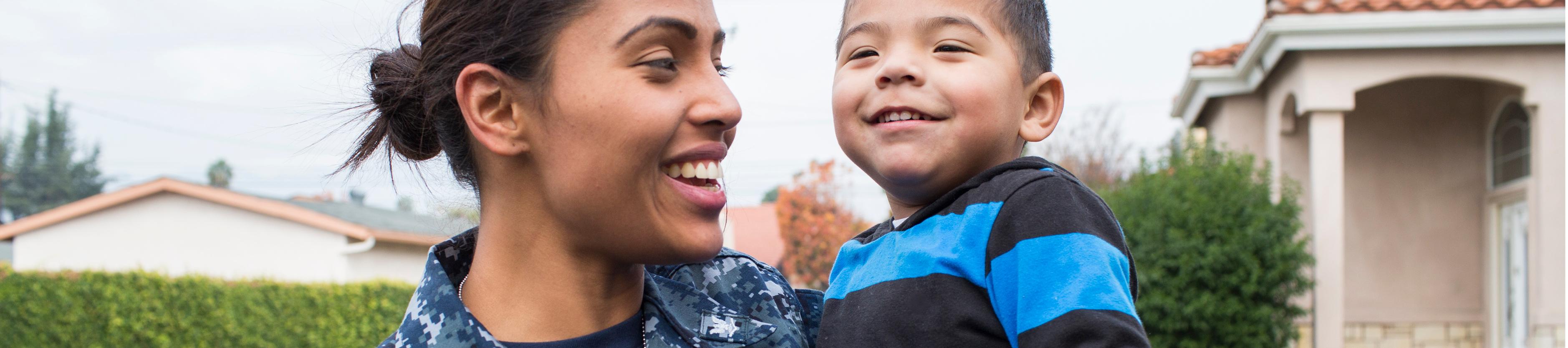 Woman in Navy fatigues holding a young boy in front of their home